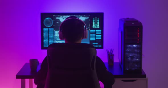 Man Programmer in Headphones Working at a Computer in Data Center at Night