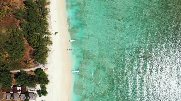 Wide fly over travel shot of a sunshine white sandy paradise beach and aqua blue ocean background in