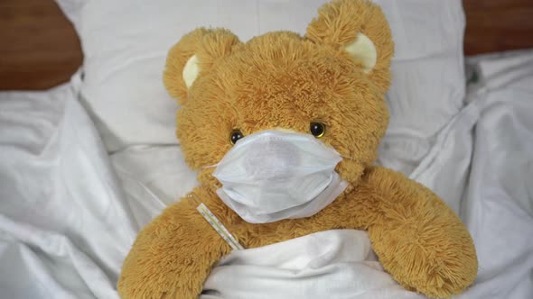 A Teddy Bear Measures the Temperature with a Mercury Thermometer. The Bear Lies in Bed with a