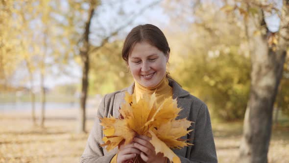 Woman in Coat Holds Autumn Leaves