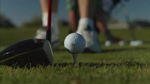 A close up of a golf ball on a tee center frame and the golfer lining up his shot with his club.