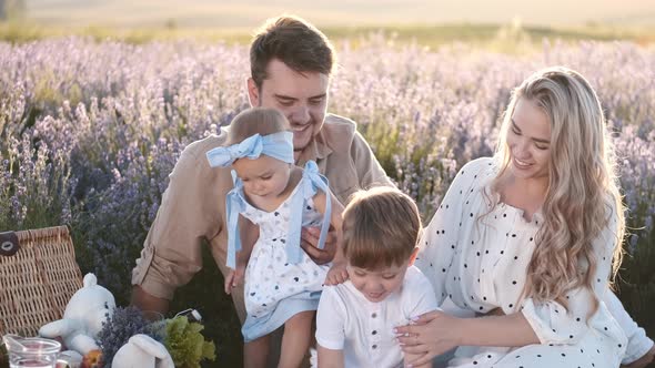 Loving Family with Kids Are Sitting on a Blanket in the Lavender Field on Sunset