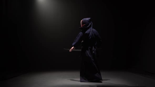 Kendo Fighter Performing Martial Art with Katana Sword at Dark Studio Under Spotlight.