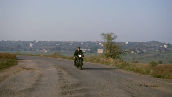 Front View of a Stylish Cool Young Man in Sunglasses and Leather Jacket Driving His Chopper on a