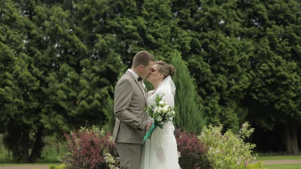 Newlyweds. Caucasian Groom with Bride Kissing in Park. Wedding Couple. Man and Woman in Love