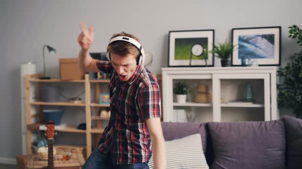 Handsome Hipster Is Having Fun in Apartment Listening To Music with Headphones Dancing and Singing