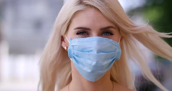 Attractive Young Blonde Woman with Blue Eyes in a Protective Medical Mask Close Up