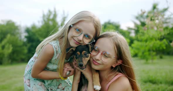 Two Girls Hug and Kiss a Small Dog Plays with Adorable Puppy Outdoors