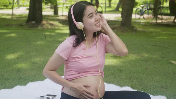 Happiness young asian woman pregnant sitting and listening music with for relaxation in the park.