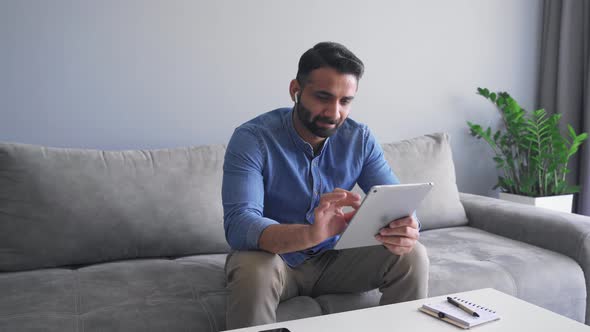 Millennial Indian Man Using Digital Tablet on Sofa and Smiling Slow Motion