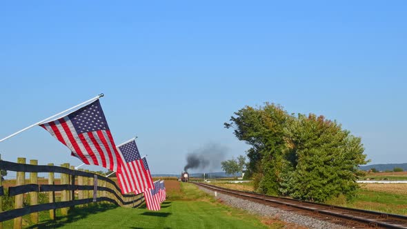 A View of a Line of Gently Waving American Flags on a Fence by Farmlands as a Steam Passenger Train