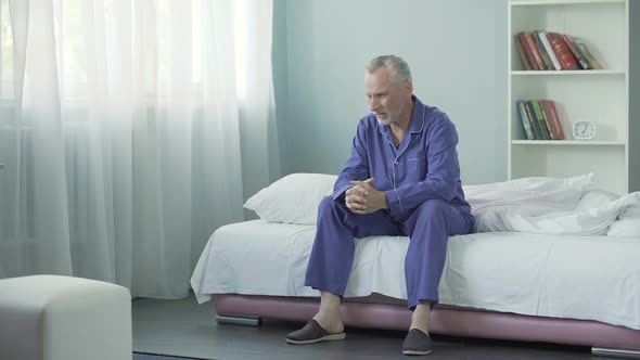 Annoyed Old Man Sitting on Bed After Awakening, Having Bad Mood in Morning
