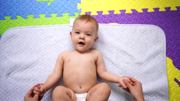 Mom Shakes and Stretches the Arms of the Lying Baby