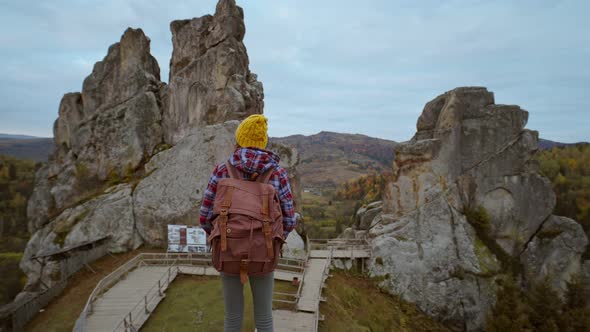 Camera Moves Around Woman Hiker with Casual Retro Backpack Sdanding on Top of a Cliff and Enjoying