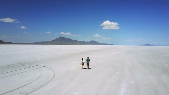 Drone Follows Romantic Couple Holding Hands, Running Towards Epic White Flat Land of Utah Salt