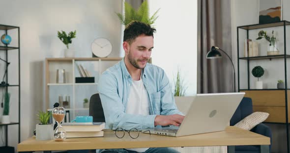 Young Man Sitting at the Table in Cozy Living-Room and Chatting with Friends on Computer