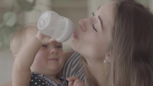 Beautiful Smiling Baby Girl Trying To Give Water To Her Mother From the Baby Bottle in the Kitchen