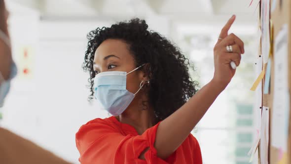 Woman wearing face mask discussing over memo notes with her colleagues at office