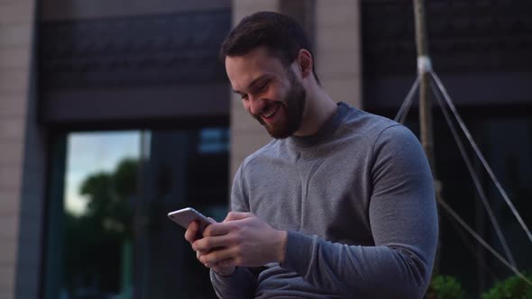 Close-up view of laughing handsome young man reading message on cell phone or watching fun video