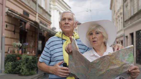 Senior Male and Female Tourists Standing with a Map in Hands Looking for Route