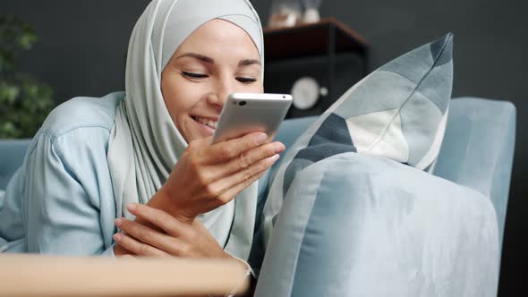 Portrait of Carefree Hijabi Woman in Scarf Recording Voice Messages and Touching Screen Messaging at