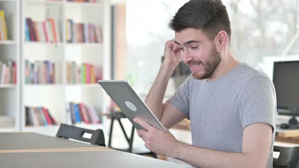 Young Man Celebrating Success on Tablet in Office 