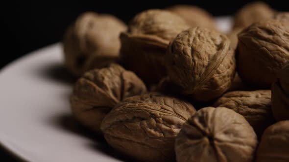 Cinematic, rotating shot of walnuts in their shells on a white surface 