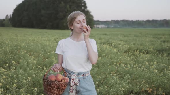 A Beautiful Country Side Girl Holding a Basket of Ripe Peaches and Sniffing Fruit