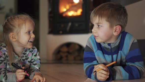 Brother and Sister Lying on the Floor in the Room Writing and Drawing Fireplace in the Background