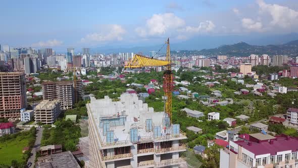 Construction crane on construction site against backdrop of mountains and city.