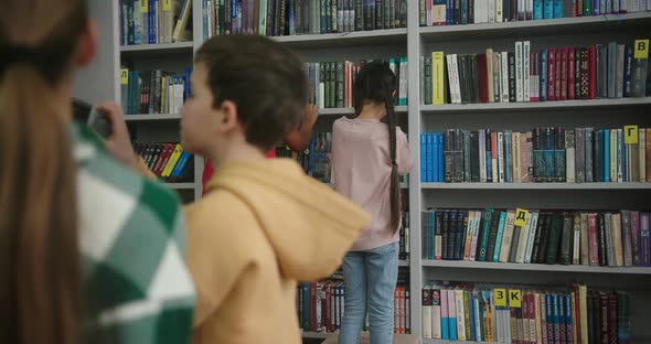 Multinational Kids Look for Books on Shelves in Library