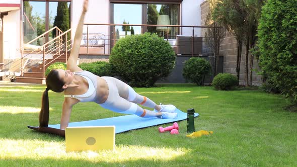 Young fitness woman in sportswear doing side plank exercise outdoors