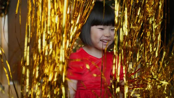 Korean Girl Child in Red Dress is Playing on Christmas Night with Golden Tinsel