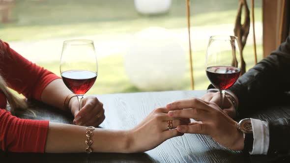 Close Up of Loving Couple Holding Hands and Clinking Glasses of Red Wine During Romantic Dinner