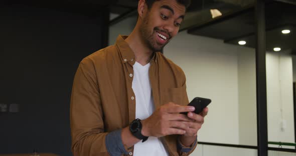 Mixed race businessman standing using a smartphone in a modern office