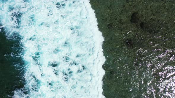 Dramatic sea scenery of big white waves splashing on shore with corals and rocks, foaming over calm