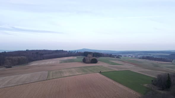 Fields and meadows bordering at bare mixed forests in Hesse, Germany. Aerial tracking shot