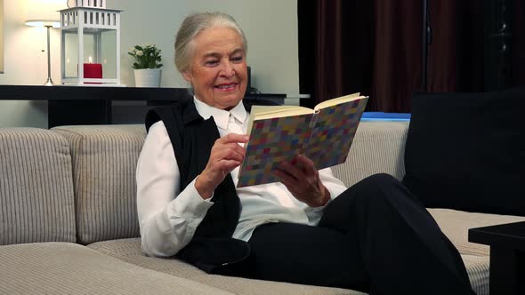 Old Caucasian Woman Reads a Book in Living Room