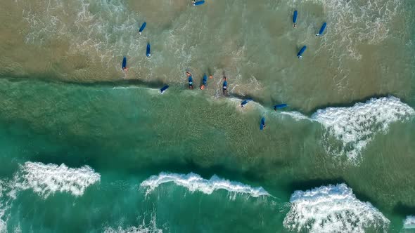 Aing drone video looking down at a large group of surfers catching waves at the beach
