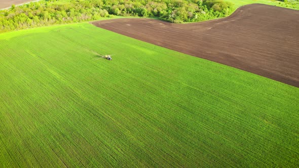 Aerial View of Farming Tractor Spraying on Field with Sprayer, Herbicides and Pesticides at Sunset