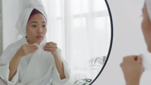 Asian Woman in Bathrobe Applying Lotion to Face