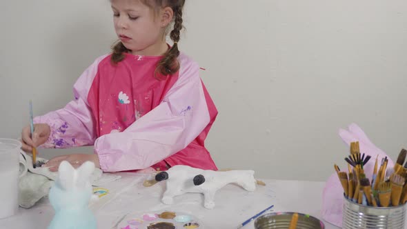 Little girl painting paper mache figurine at homeschooling art class.