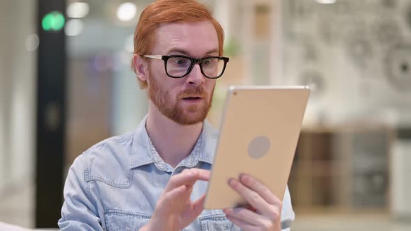 Young Redhead Man Celebrating Success on Tablet