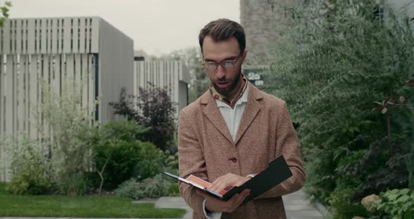 Unhappy Bearded Man in Glasses Holding Folder While Reading Finance Documents