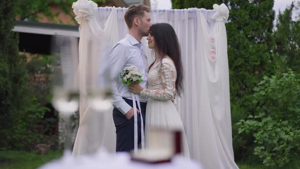 Confident Loving Interracial Couple Kissing Rubbing Noses Standing at Wedding Altar in Spring Garden