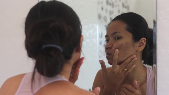 Young asian woman checking her face covered with acne , bathroom scene in front of a mirror.