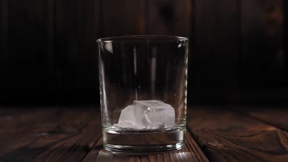 Close-up of Ice Cubes Falling Into an Empty Glass on a Dark Wooden Background