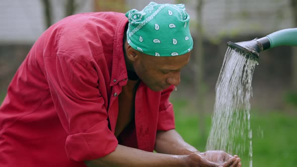 Young African American Man Washing Face with Water in Garden After Work