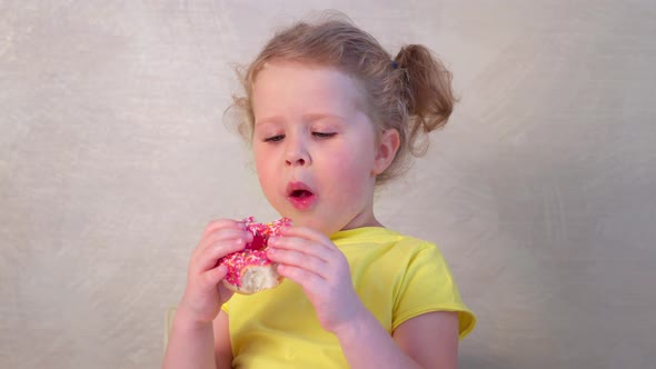 Little caucasian girl eats an appetizing donut and licks her fingers with pleasure