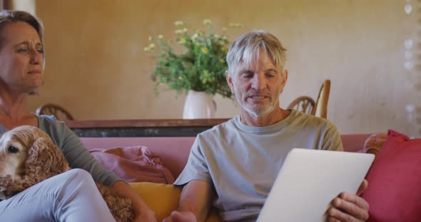 Senior caucasian couple using tablet and sitting with dog in living room